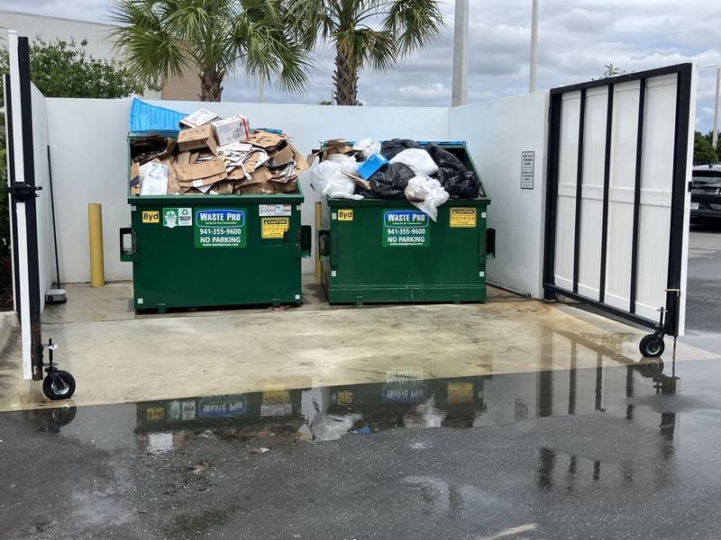 The same dumpster enclosure after washing, with the litter gone and the concrete pad clean and wet