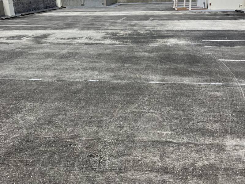 Top deck of a parking garage, dark gray and blotchy with tire tracks, before pressure washing