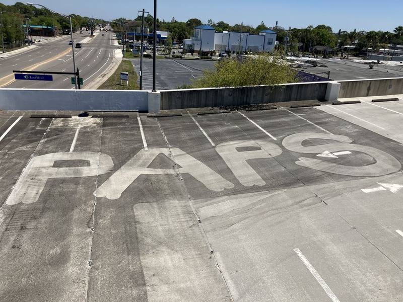 Garage deck partly cleaned, with the letters PAPS cleaned into the darker dirty concrete