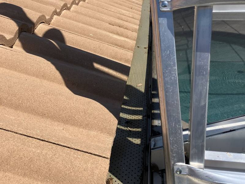 The roof edge and perforated gutter guard cleared of leaves after cleaning, with a ladder in frame