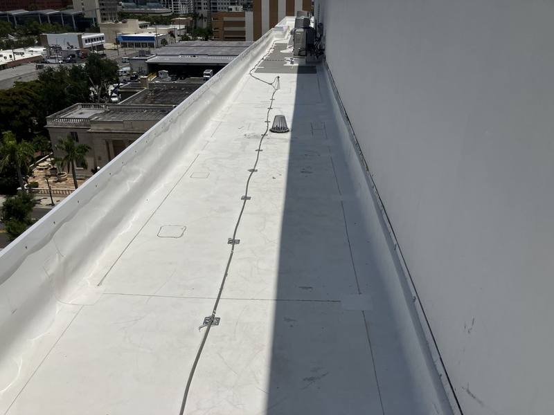 Flat commercial roof with a clean bright white surface beside a tall wall, with city buildings beyond the roof edge