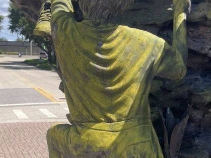 Bronze statue of a child climbing rocks, covered in a yellow-green film