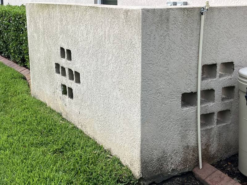 Stucco wall with decorative block openings, stained gray and streaked dark near the base, before soft washing